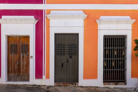 Detailed view of traditional wooden doors and a window with iron grilles on vibrant pink and orange