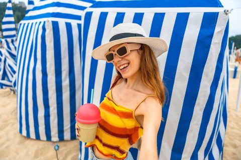 Woman smiling brightly and holding an ice cream shaped cup with a drink, wearing sunglasses and a