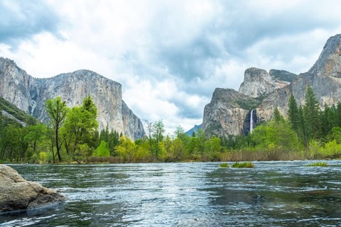 Merced river flowing through yosemite valley, surrounded by towering el capitan granite walls, lush