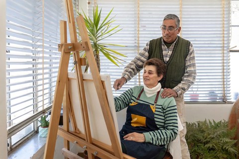 Senior couple standing together and looking at a canvas on an easel in a bright home art studio