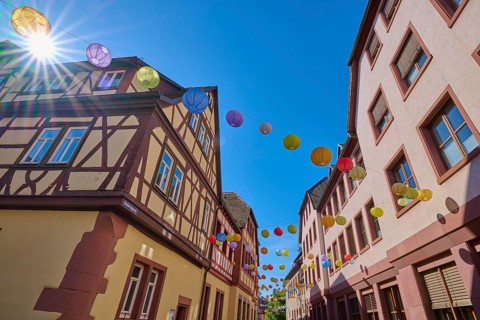 Sunbeams flood a street with half-timbered houses and colorful lanterns, Lohr am Main,