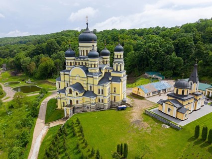 Orthodox monastery with yellow paint and domes surrounded by green landscape, aerial view, Hîncu