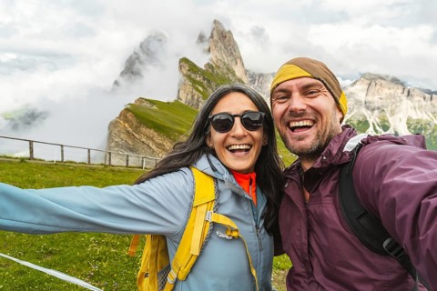 Cheerful couple of hikers friends taking selfie in Dolomites mountains.Millennial guy girl enjoying