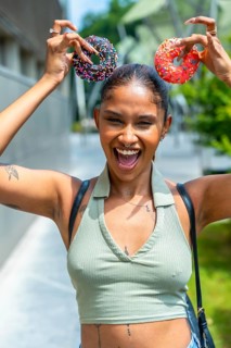 Smiling young woman making a funny face, holding two colorful sprinkle donuts like ears over her