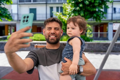 Happy father holding his young son and smiling while using a smartphone to capture a selfie