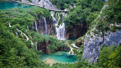 Multi-level waterfalls flow into turquoise water surrounded by thick vegetation and rocks, Plitvice