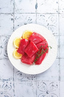 Fresh tuna slices, on a white plate, with lemon slices and herbs, top view, no people