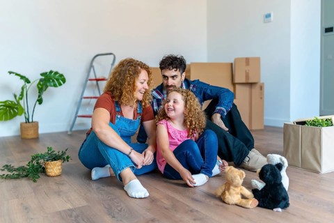 Happy family sitting on the floor in a new empty house, chatting and bonding while surrounded by