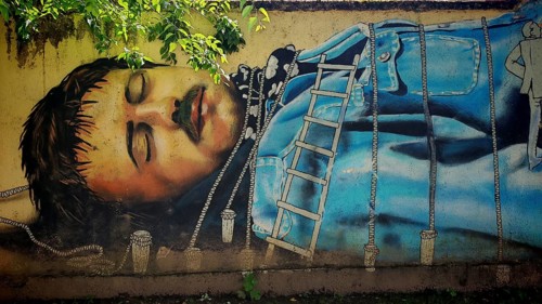 A mural depicts Guliver a man in a blue robe with ropes in a natural setting, Zagreb, Croatia