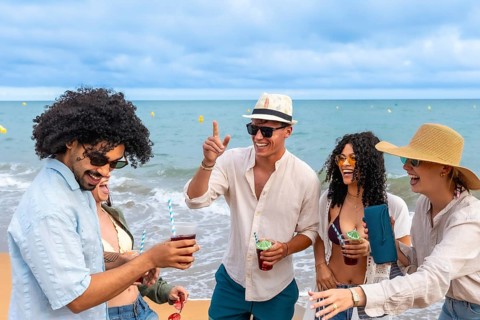 Group of diverse young adult friends laughing and talking, holding colorful cocktails and a