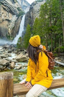 Woman with backpack and yellow jacket sitting on a wooden fence, looking towards the powerful lower