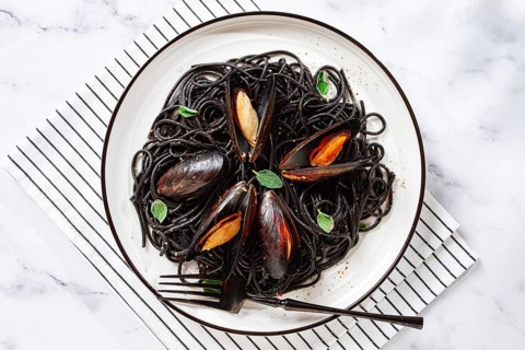 Black spaghetti with mussels, on a white plate with a fork, on a striped napkin, marble background,