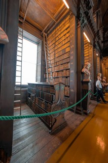Historic library with tall bookshelves, wood paneling and a statue, Trinity Collage, Dublin,