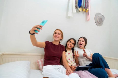 Teenage girl holding smartphone, capturing a moment with her two younger sisters making funny faces
