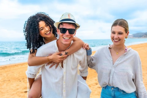 Diverse group of young adults laughing and hugging on a sunny beach, enjoying a carefree summer