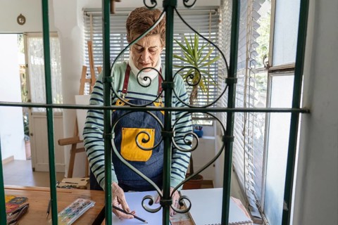 Creative framing of a mature female artist sketching at her art table, photographed through an