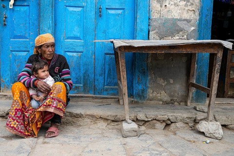 Elderly Nepalese woman with grandchild sitting in front of her house, Hindu ethnic group,