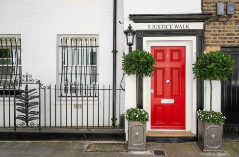 Classic red door with black frame and plants on both sides, white house facade, 5 Justice Walk,