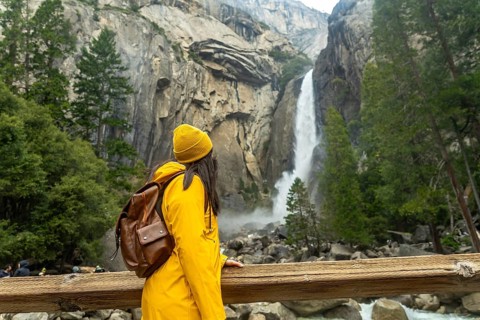 Woman wearing yellow jacket and knit hat admiring the powerful lower yosemite fall, witnessing the