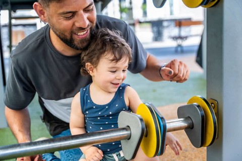 Happy father and son enjoying time together outdoors at a playground, the father supporting his