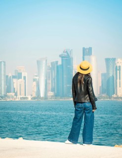 Woman wear casual clothing yellow hat overlooking Doha West Bay skyline. Visible landmarks: Burj