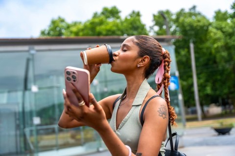 Young woman standing outdoors, wearing a casual outfit, enjoying a takeaway coffee while actively