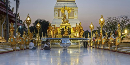 Altar with Buddha statues in front of the chedi decorated with golden ornaments in Wat Phra That