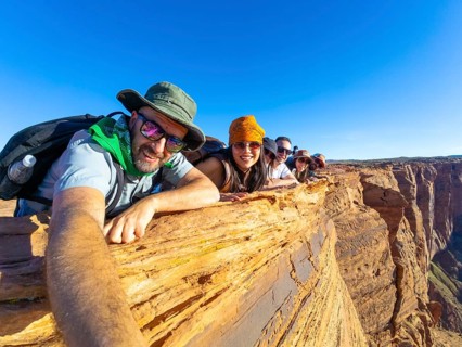 Group of diverse friends lying down on a cliff edge, smiling at the camera, enjoying travel and