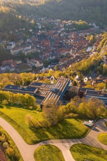 Aerial view of a settlement with traditional houses surrounded by green hills and sunlight, Calw