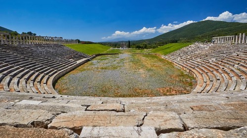 Old stone stadium surrounded by green hills and blue sky, Messene Stadium, Ancient Site,