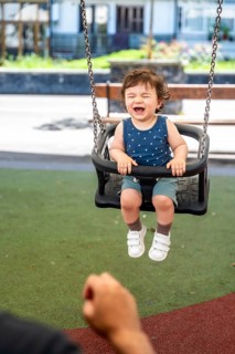Cheerful baby boy laughing on a swing at a sunny playground, bonding with a parent while enjoying