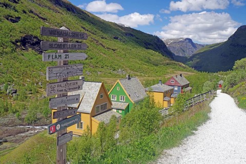 Colourful houses on a hillside with signs and a path in a mountainous green landscape, Rallarveien,