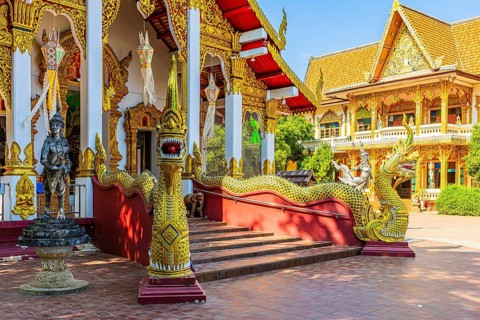 Richly decorated public prayer hall, in front of a staircase with dragon-like beings, in the Wat