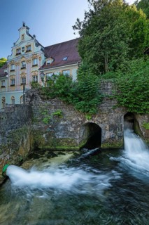 Water flowing from historic stone channels at the Brenzursprung karst spring, with a baroque town