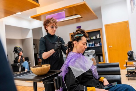 Professional hair stylist wearing gloves and apron carefully applying hair color to a female