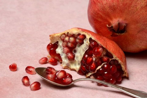 Opened pomegranate and pomegranate seeds in a spoon, Punica granatum