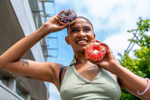 Happy young woman holding two frosted donuts with sprinkles, smiling sweetly and looking up,