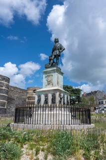 Bronze statue of King René on a decorated stone base in the foreground in front of one of the