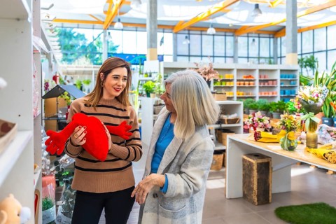 Two women of different generations browse a bright garden center, smiling and chatting as they