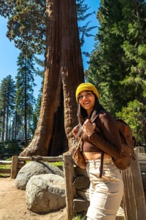 Happy young woman wearing a yellow beanie and backpack, smiling while exploring the majestic giant