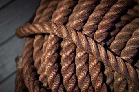 Close-up, thick rope on wooden floor, illuminated in contrast between light and shadow,