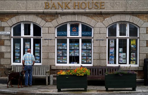 Man standing with his dog in front of Bank House, former bank, now real estate agent, St Just in