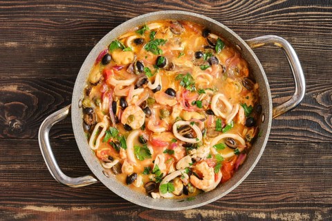 A pan contains a seafood dish with shrimp, squid, mussels and various vegetables. The meal is