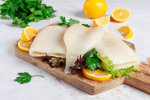 Fresh squid prepared for cooking, surrounded by herbs and lemon, placed on a wooden chopping board