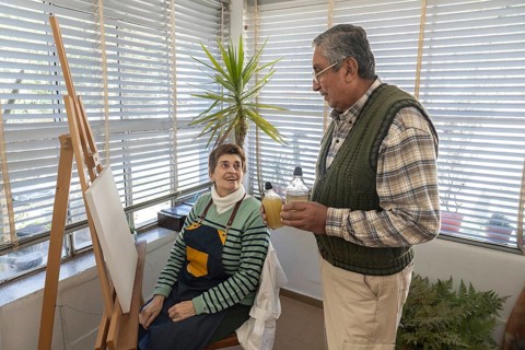 Senior couple preparing art supplies beside a blank canvas in a bright home art studio before
