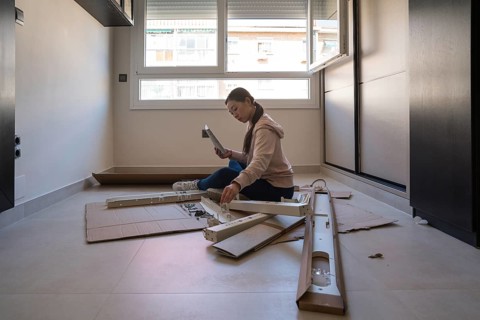 An Asian woman is focused on assembling a white desk at home, engaged in a DIY furniture project.