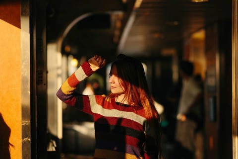 A woman stands inside a ferry wearing a colorful striped sweater in New York. Golden sunlight