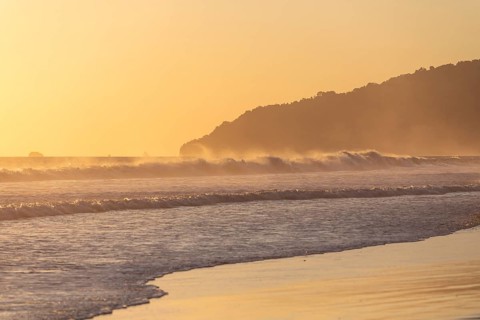 The low sun's golden light illuminates the ocean spray on Carate Beach, with views of Corcovado NP