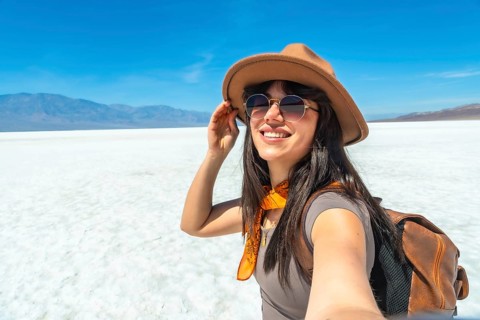 Happy young woman tourist enjoying a desert journey, smiling while taking a selfie at badwater