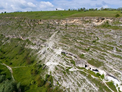 Limestone cliffs with caves and grass on a steep wall under blue sky, aerial view, cave dwellings,